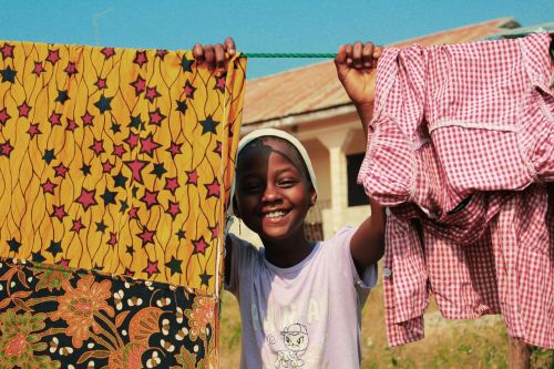 A cheerful young girl hangs colorful laundry on a sunny summer day.