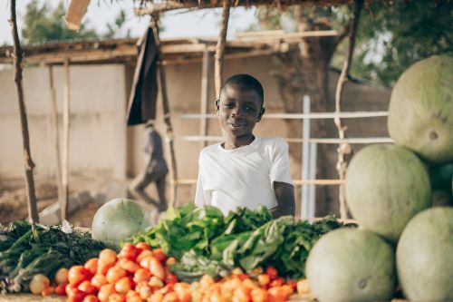 A young boy at an outdoor market stall with fresh produce, captured in a rural setting.