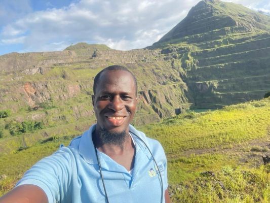 African woman in pink shirt carrying a donation box outdoors in Lagos, Nigeria.